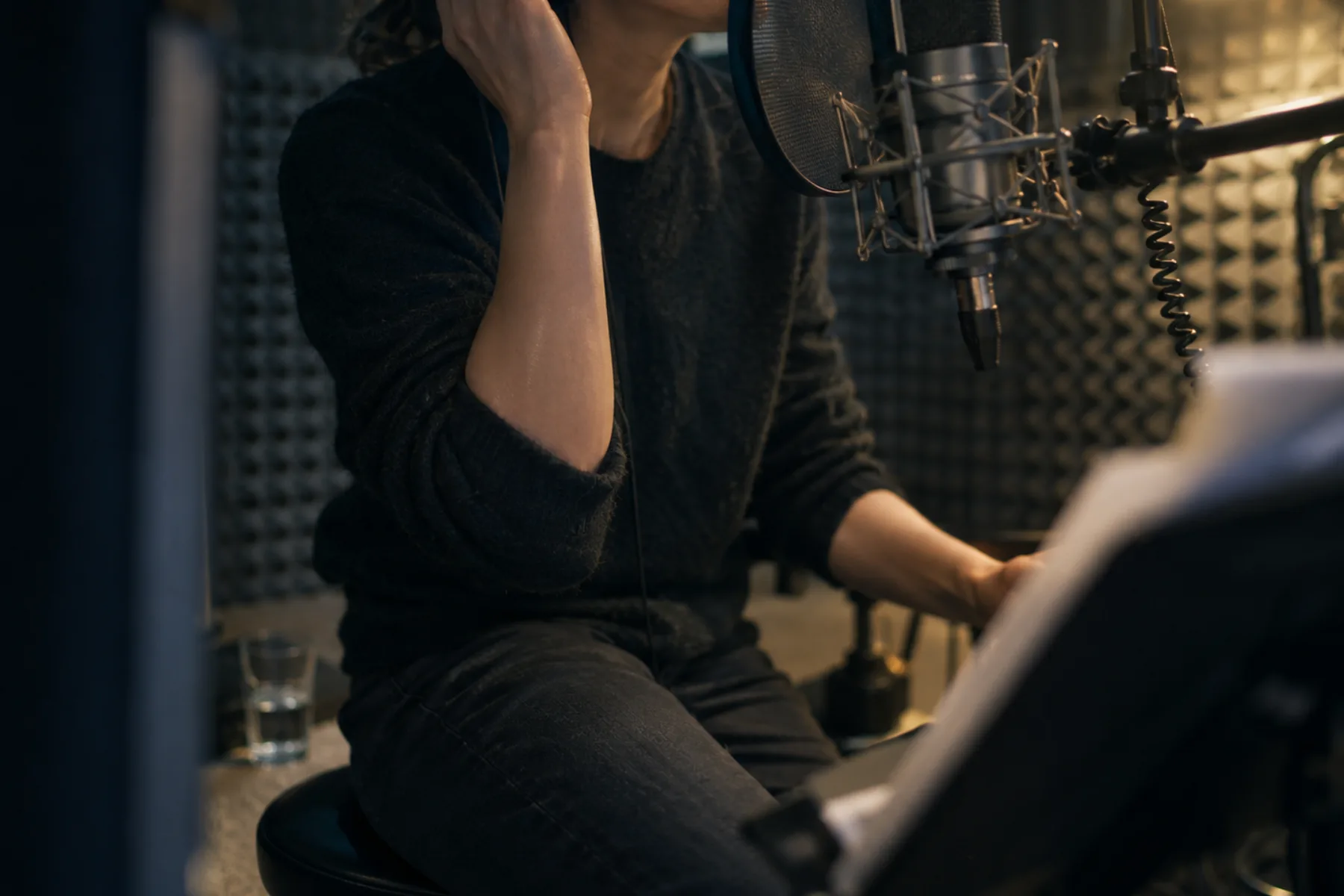 Person recording an advertising voiceover into a studio microphone in a small padded booth